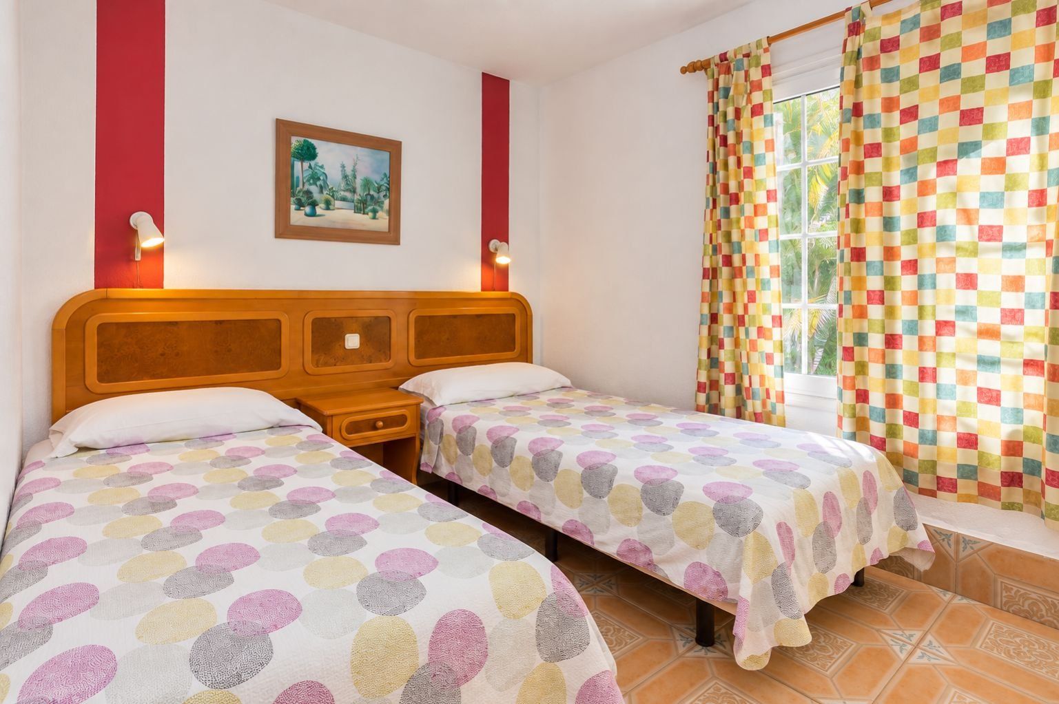 Una habitación con dos camas, un cuadro en la pared, una ventana con cortinas y una mesita de noche.
