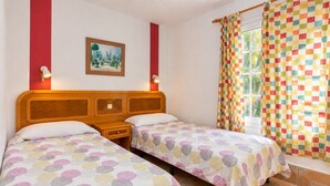 Habitació amb dos llits, un quadre a la paret, una finestra amb cortines i una petita taula de nit.
