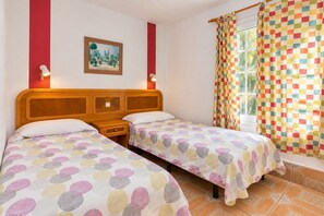 Quarto com duas camas, um quadro na parede, uma janela com cortinas e uma mesinha de cabeceira.