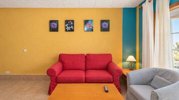 A living room with a red sofa, a grey armchair, a wooden coffee table, and four framed floral paintings on the wall.