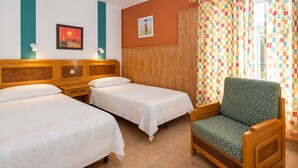 Habitació d'hotel amb dos llits, un capçal de llit de fusta, una butaca verda, una cortina multicolor a quadres i una paret amb una pintura de paisatge al capvespre.