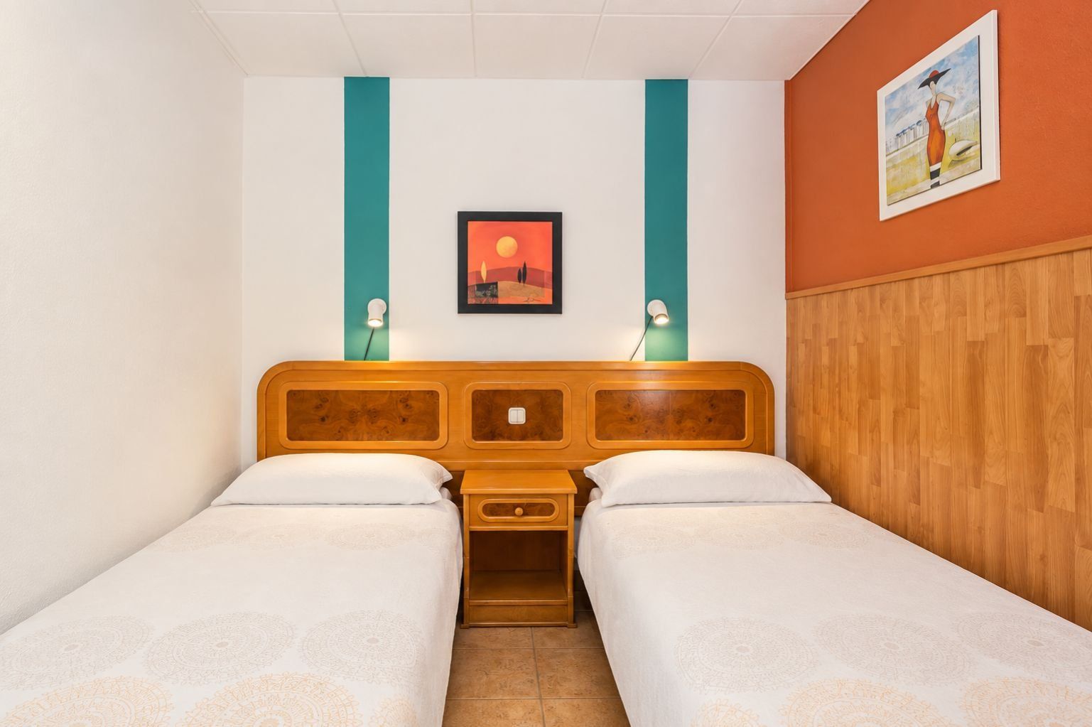 Habitación doble con dos camas, cabecera de madera, mesita de noche y un cuadro colgado en la pared.