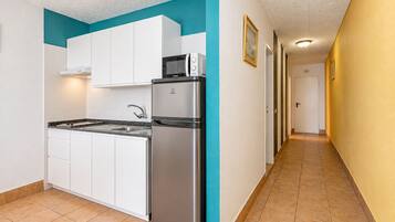 Una cocina compacta con muebles blancos, un refrigerador de acero inoxidable y un microondas.