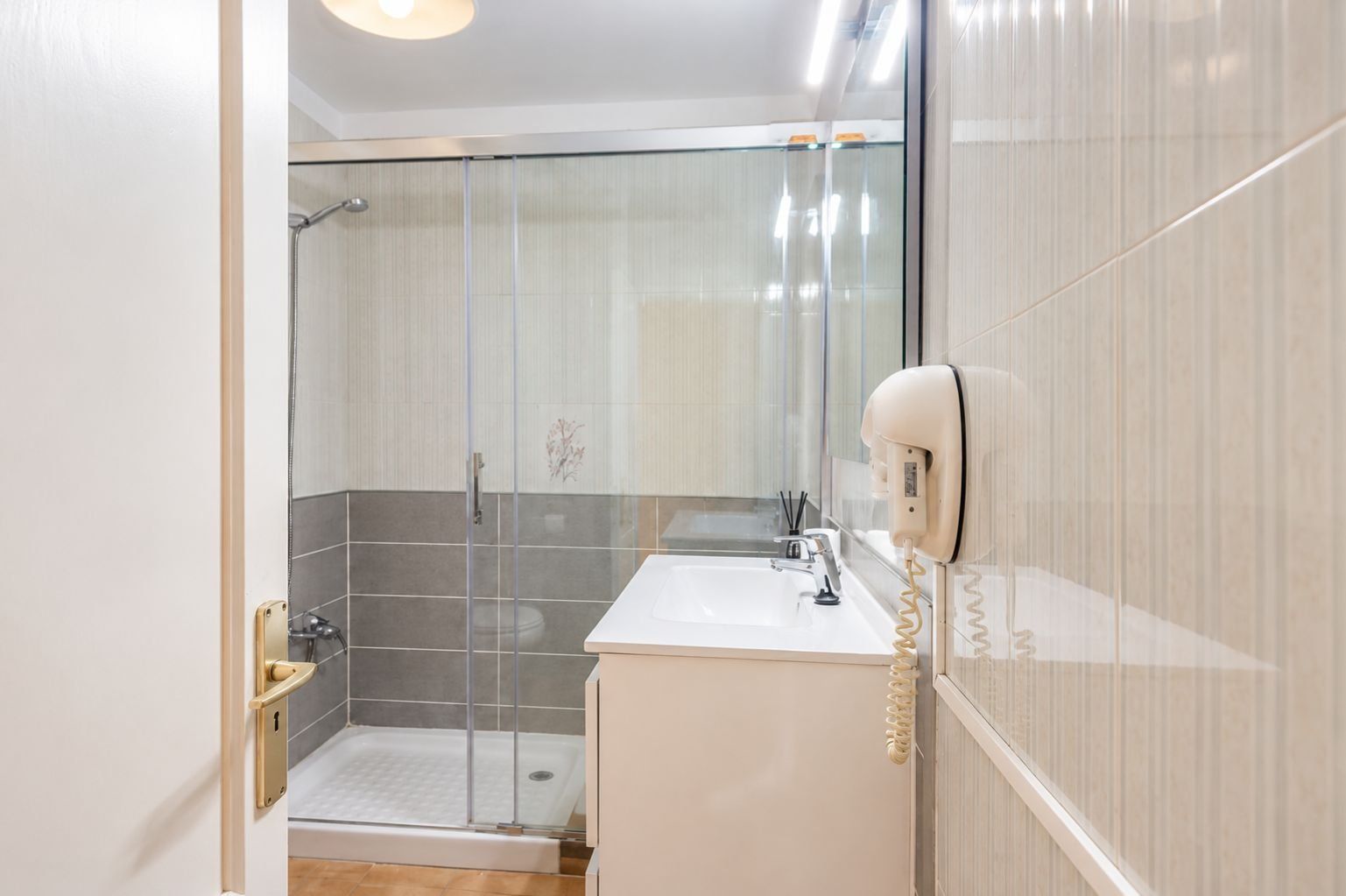 Un baño moderno con cabina de ducha de vidrio, lavabo blanco y un secador de pelo montado en la pared.