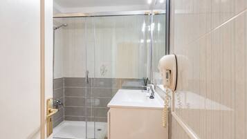 Un baño moderno con cabina de ducha de vidrio, lavabo blanco y un secador de pelo montado en la pared.