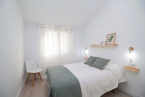 Een slaapkamer met een bed, een stoel, een nachtkastje en een wandplank.