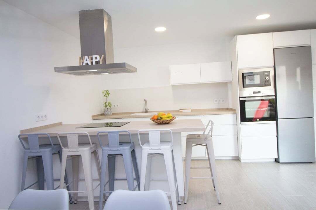 A modern kitchen with a central island, bar stools, a stainless steel refrigerator, and a microwave.