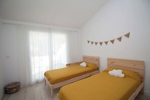 A room with two beds, a window with sheer curtains, a small round table, and a wall-mounted bunting decoration. - GuestReady - Valdelagrana 4 Diana (El Puerto de Santa María)