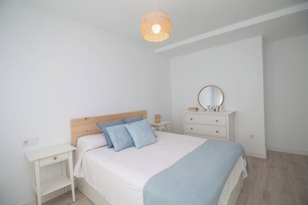 A bedroom with a bed, bedside table, dresser, and a hanging light fixture.