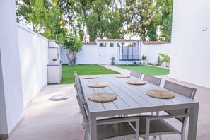 Eine Terrasse mit Tisch und Stühlen, umgeben von einer weißen Mauer und einem kleinen Garten.