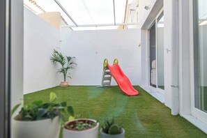 A small indoor space with artificial grass, a red slide, and potted plants. - GuestReady - Valdelagrana 4 Diana (El Puerto de Santa María)