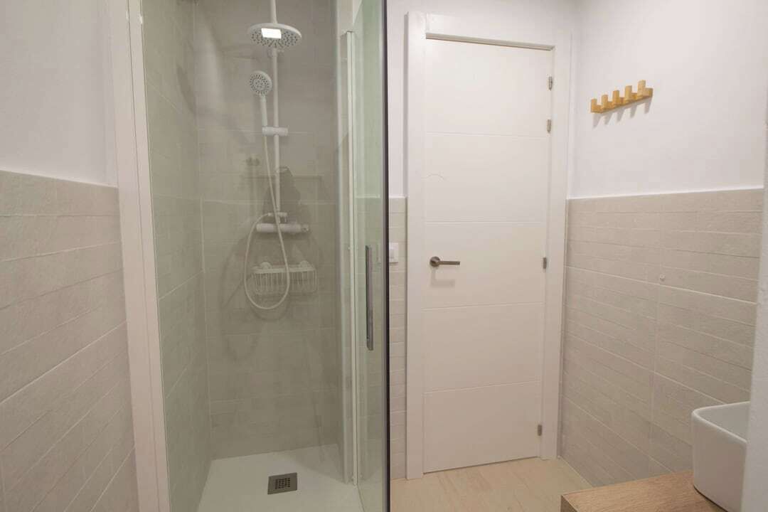 A bathroom with a glass-enclosed shower, a white door, and a wooden shelf with toiletries.
