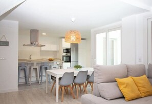 A modern kitchen with white cabinetry, a dining area with a white table and grey chairs, and a sofa with a yellow pillow. - GuestReady - Valdelagrana 4 Diana (El Puerto de Santa María)