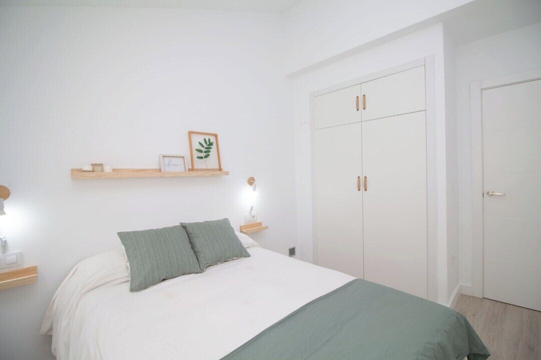 Un dormitorio con cama, mesitas de noche, armario y estantes con marcos.