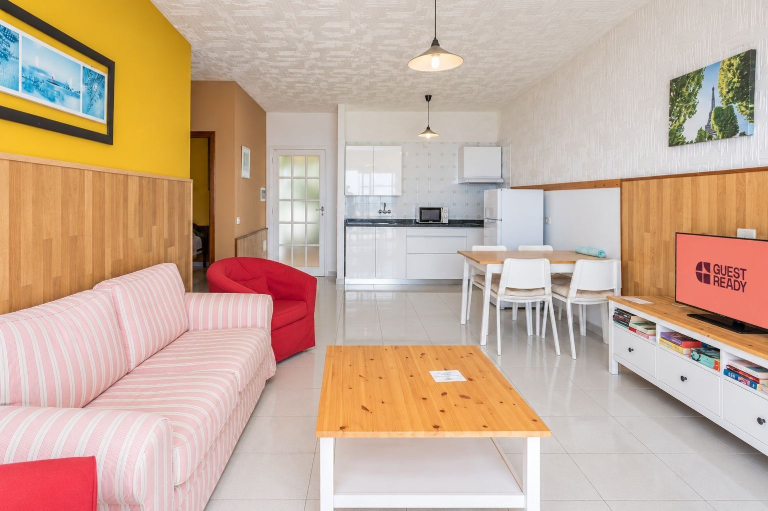 Een moderne woonkamer met een bank, een rode fauteuil, een houten salontafel en een televisie.