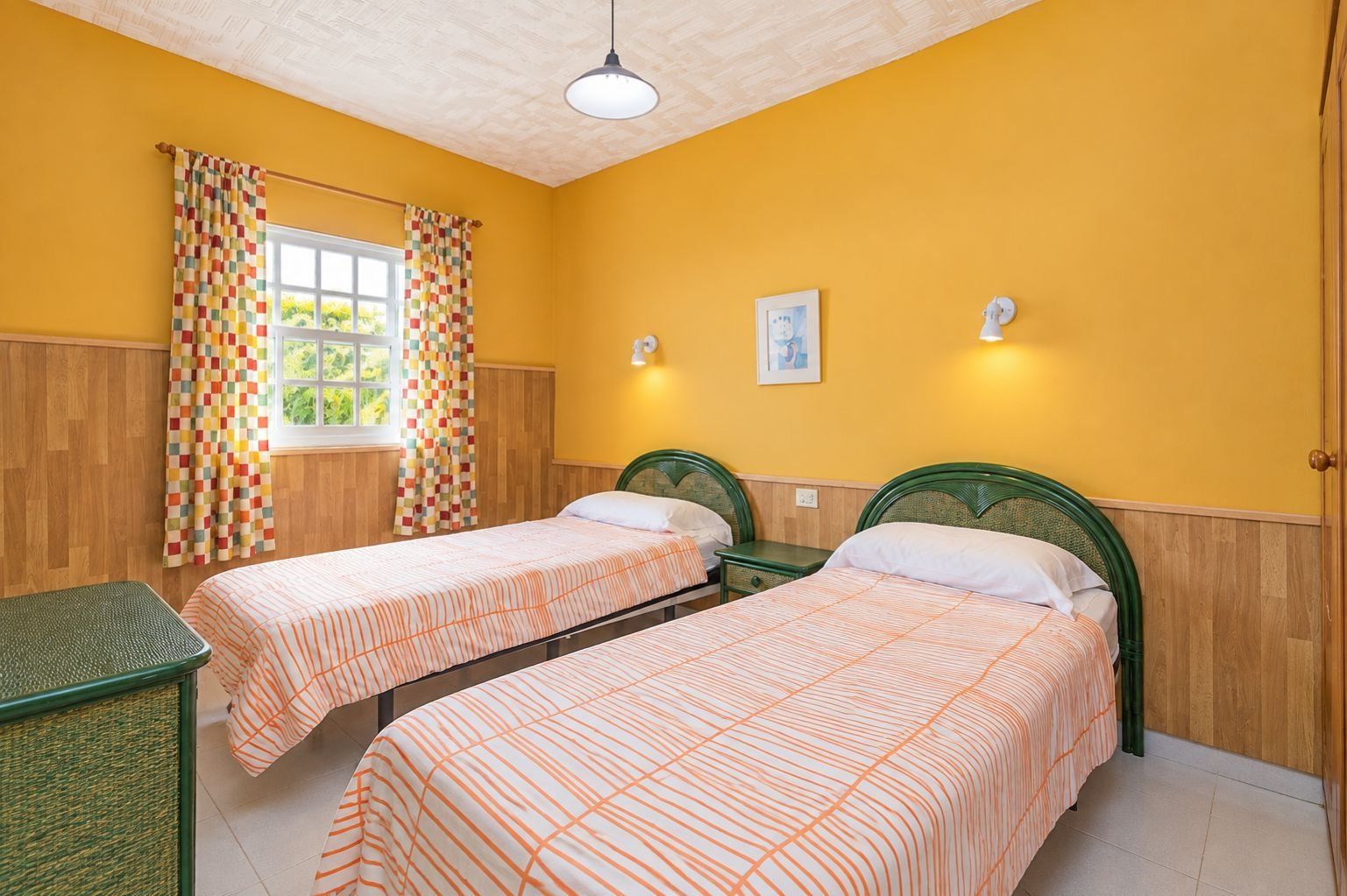 A room with two single beds, wooden paneling, a window with curtains, and a small table.