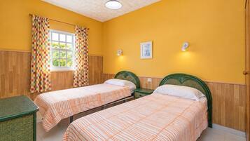 A room with two single beds, wooden paneling, a window with curtains, and a small table.
