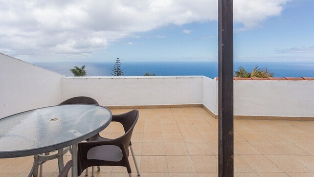 Un balcó amb taula i cadires de vidre, amb vista al mar.