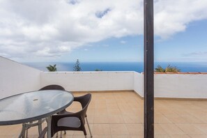 Un balcón con una mesa y sillas de vidrio, con vistas a la costa.