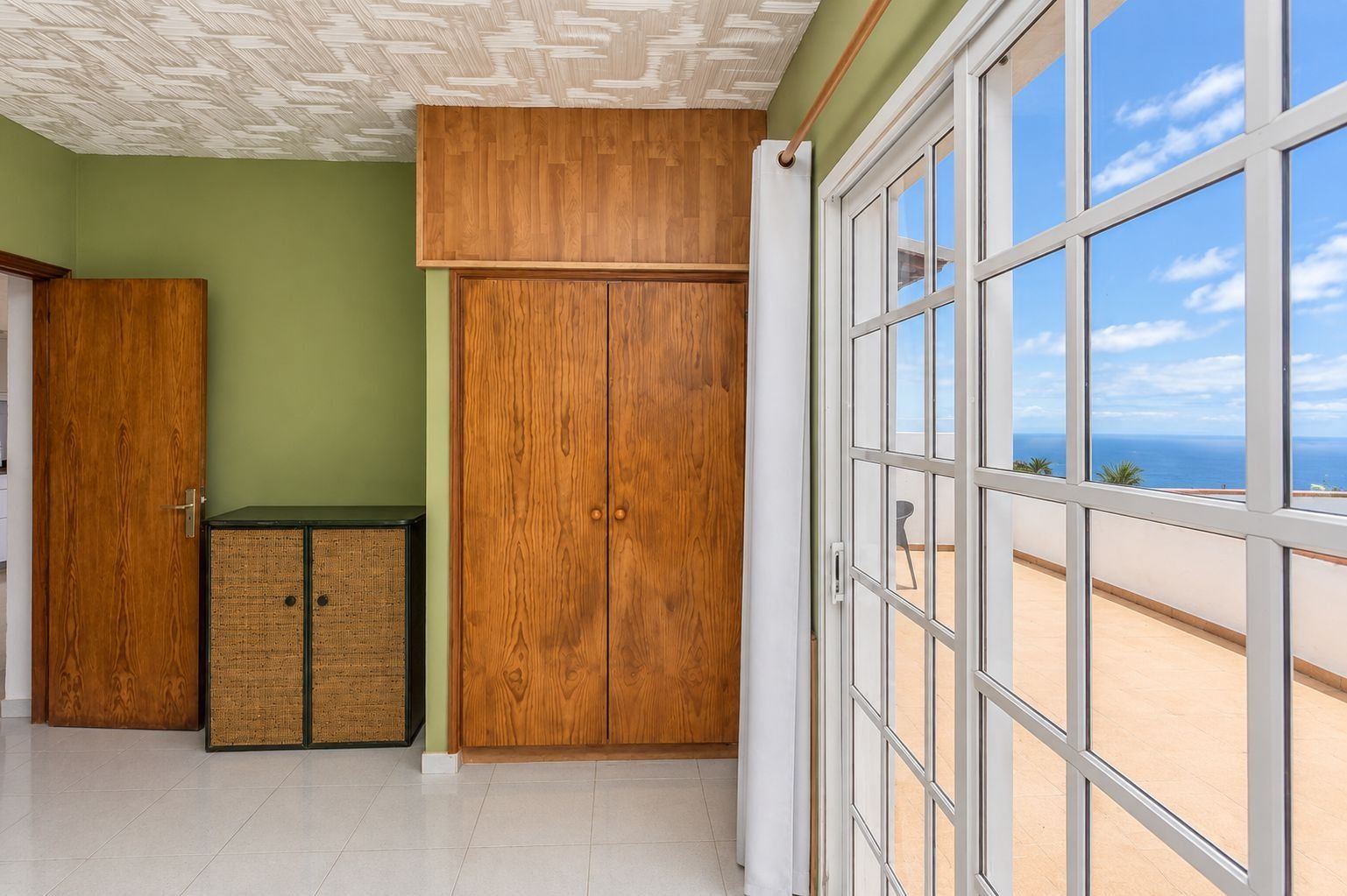 Una habitación con un ventanal grande, un armario de madera y una puerta.
