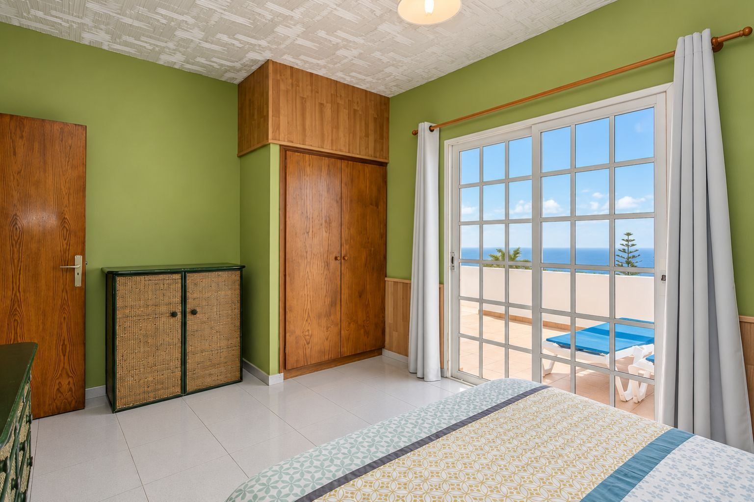 Una habitación con un gran ventanal corredizo que da a un balcón con vista a la piscina.
