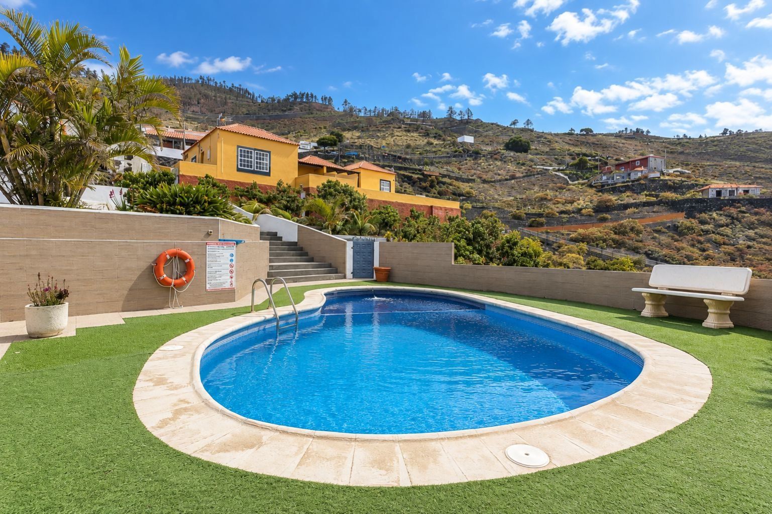 Una piscina con un flotador salvavidas, escaleras y vistas a casas en una ladera.