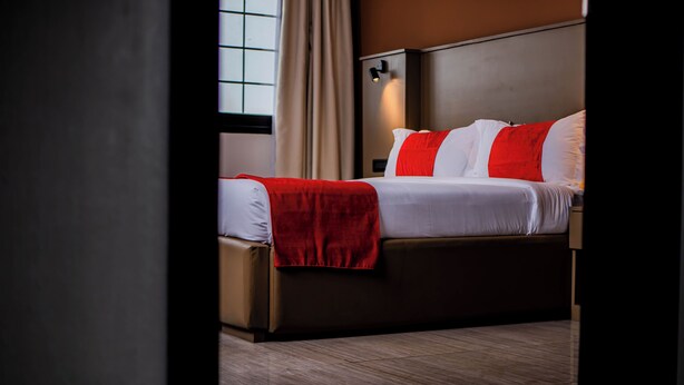 Una habitación de hotel con cama, mesita de noche y ventana con cortinas.