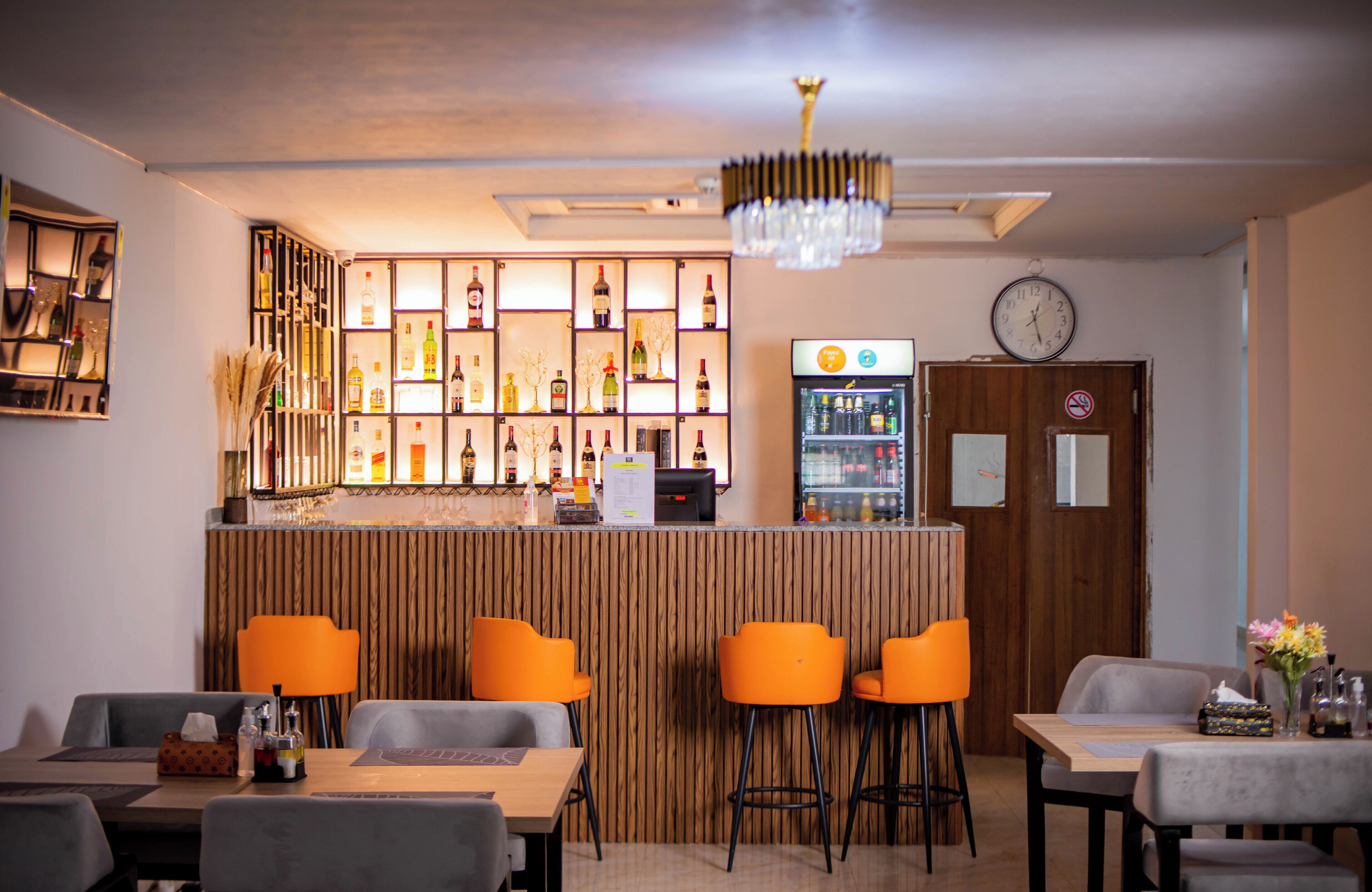 A bar area with a wooden counter, multiple stools, and a variety of bottles and glasses.