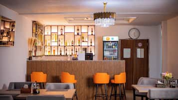 Zona de bar con mostrador de madera, varios taburetes y una variedad de botellas y vasos.