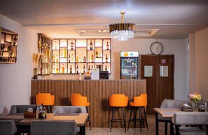 Zona de bar con mostrador de madera, varios taburetes y una variedad de botellas y vasos.