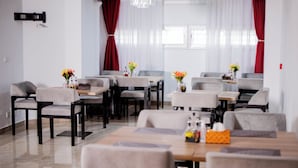 Un comedor moderno con varias mesas y sillas, una araña y cortinas rojas.