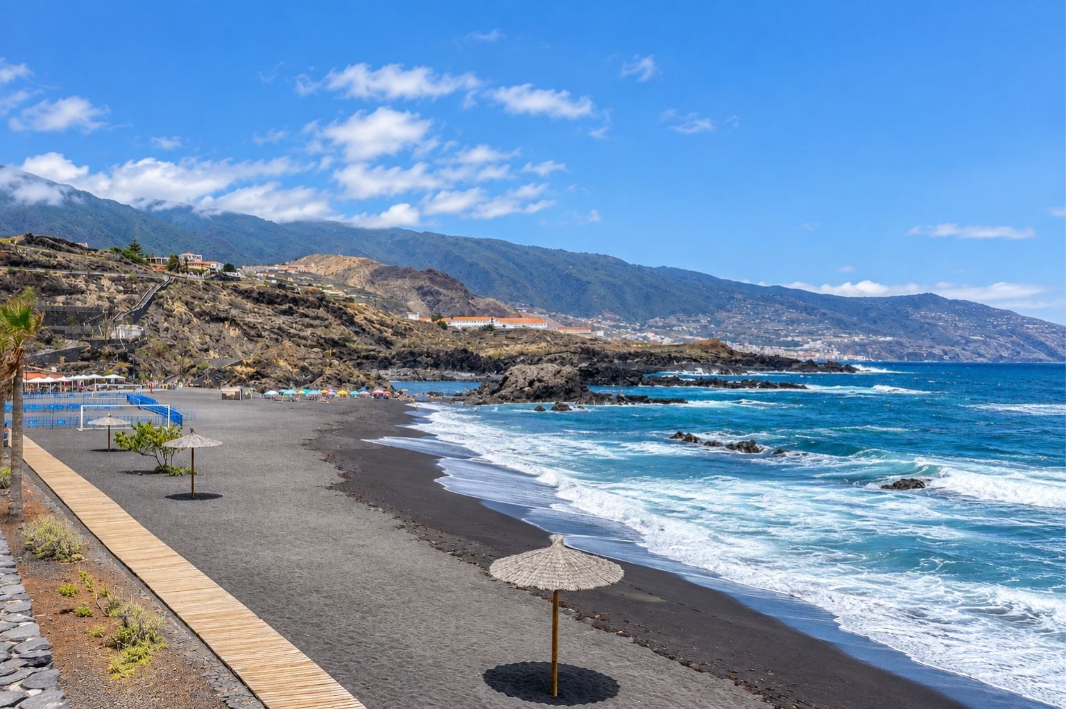 A beach with a wooden walkway, umbrellas, and rocky coastline.
