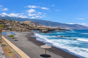 Una playa con un paseo de madera, sombrillas y un litoral rocoso.