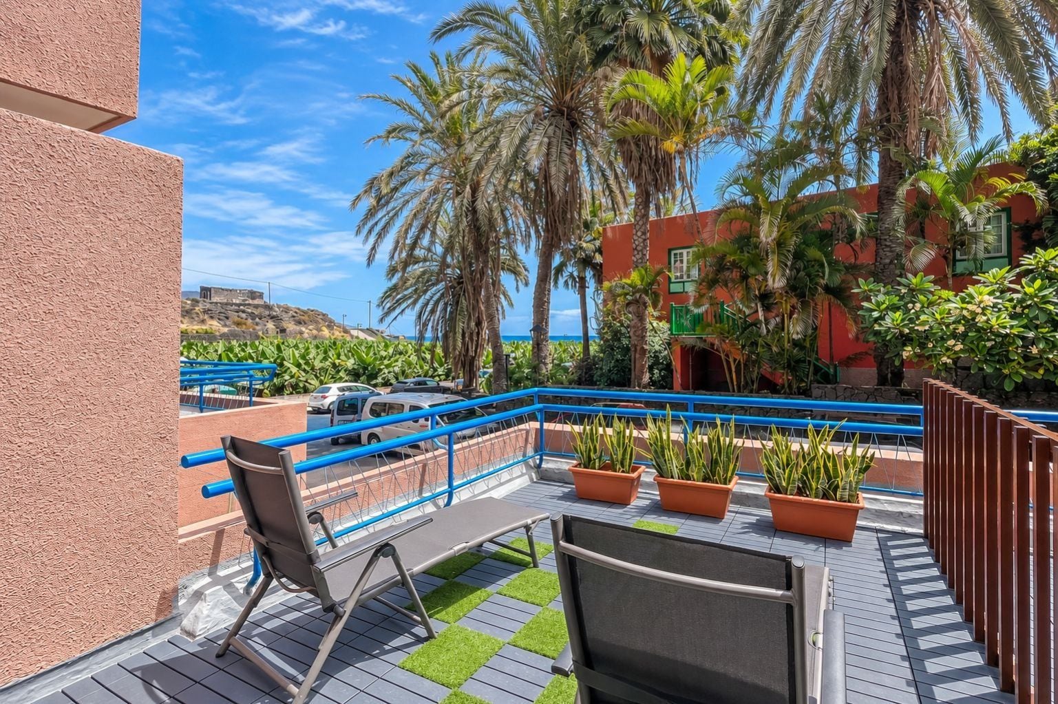 A balcony with a blue railing, a chair, and potted plants.