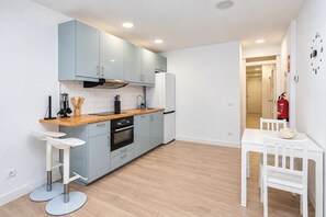 Una cocina moderna con armarios azul claro, encimera de madera y horno empotrado. Hay una mesa de comedor blanca con sillas y un reloj de pared blanco.