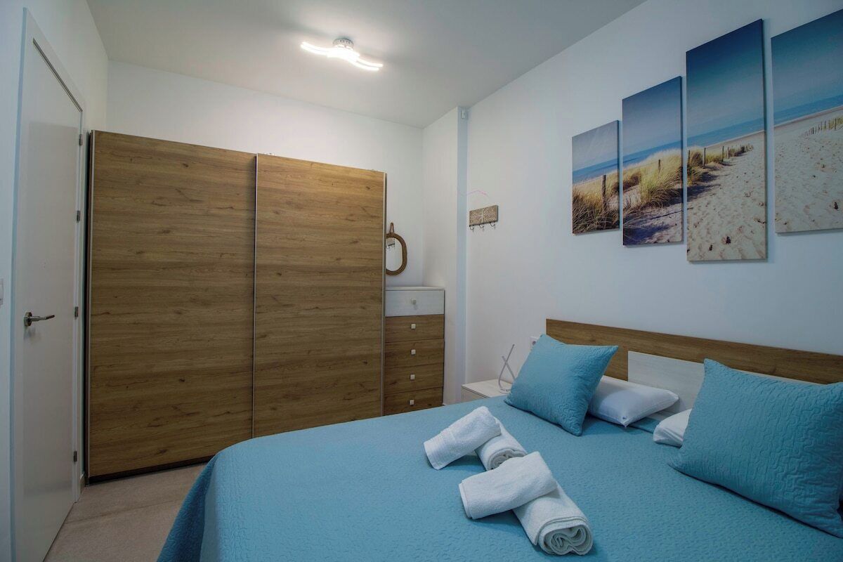 A bedroom with a bed, blue bedding, a wooden wardrobe, and beach-themed wall art.