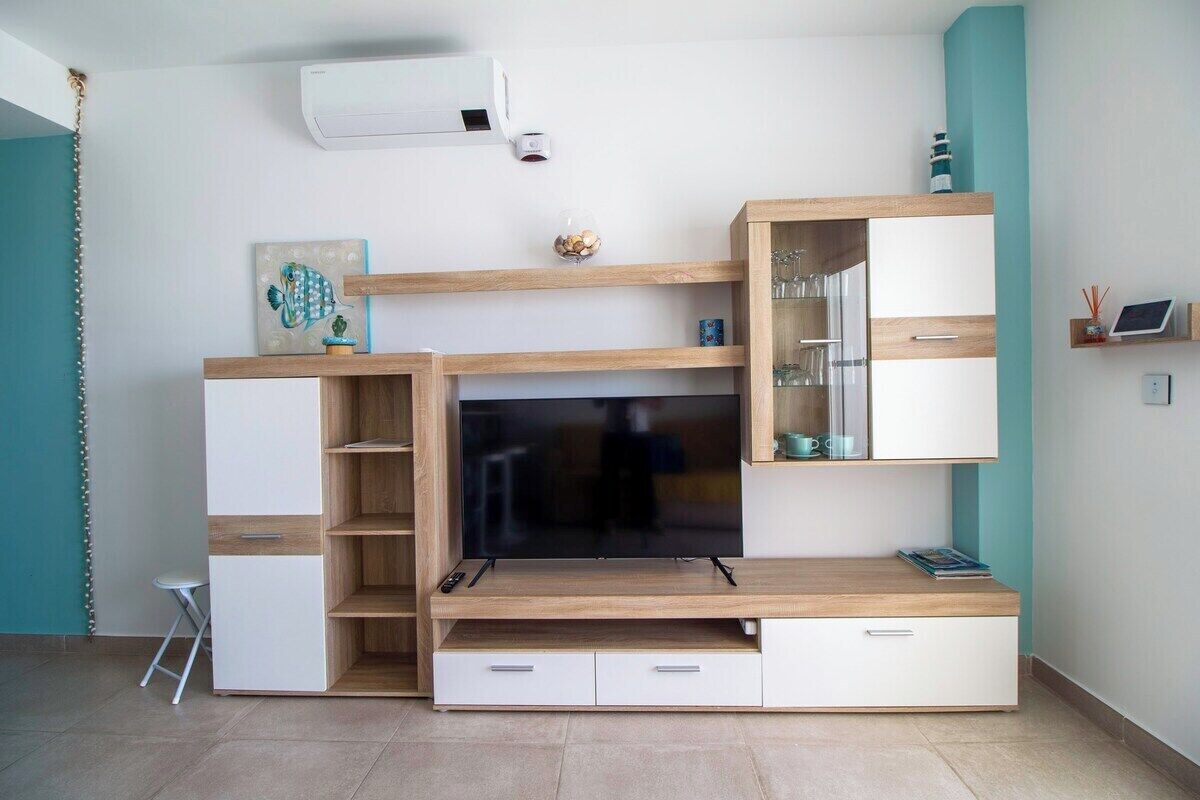 A modern living room with a built-in TV, wooden shelves, and a small seating area.