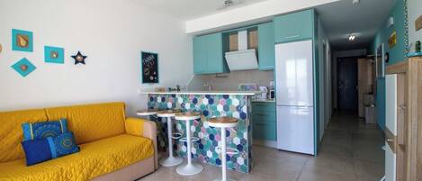 A compact living space with a yellow sofa, a kitchenette with teal cabinets, and a small bar area with stools.