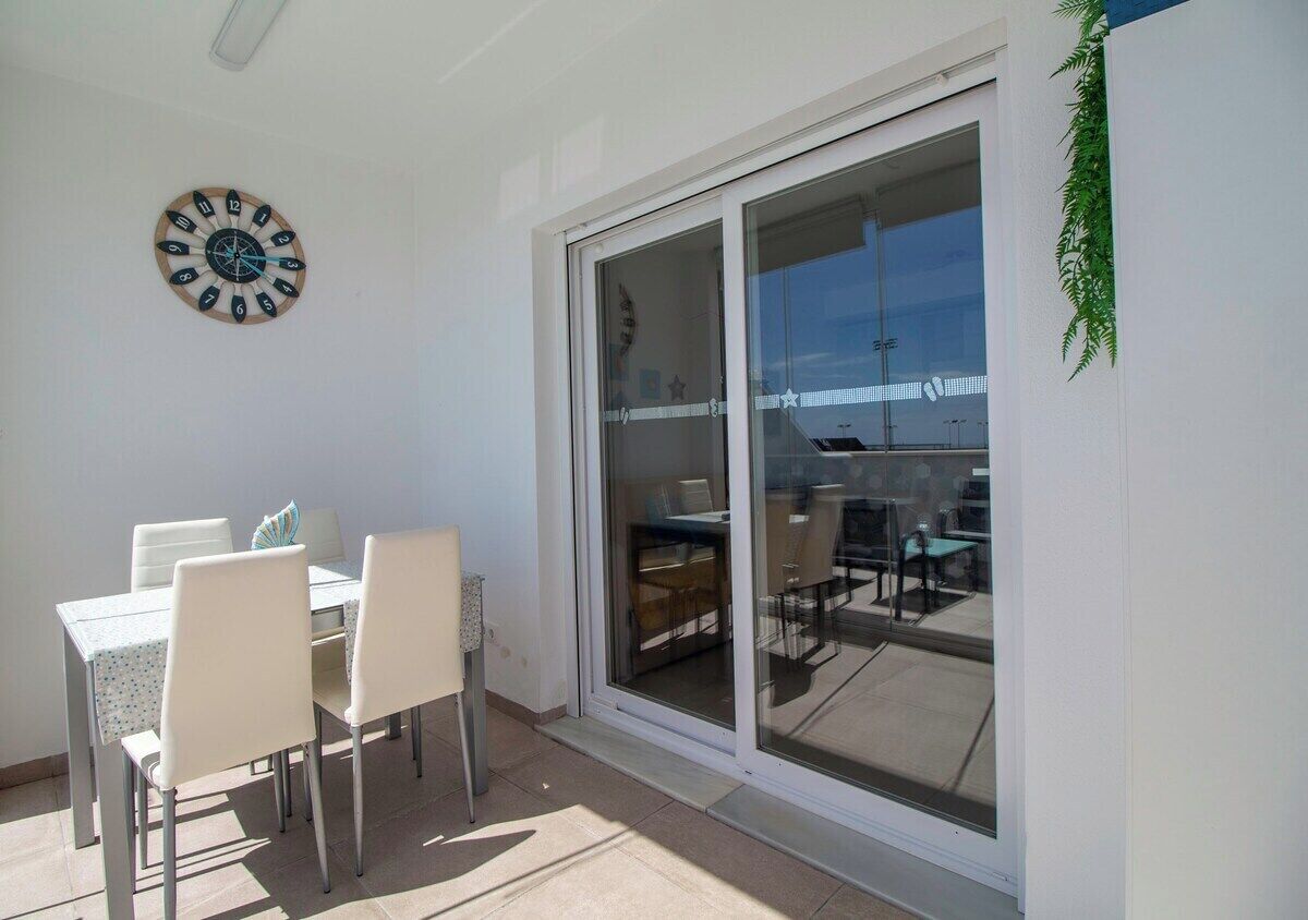 A patio with a table and chairs, a wall clock, and a sliding glass door leading to an outdoor area.
