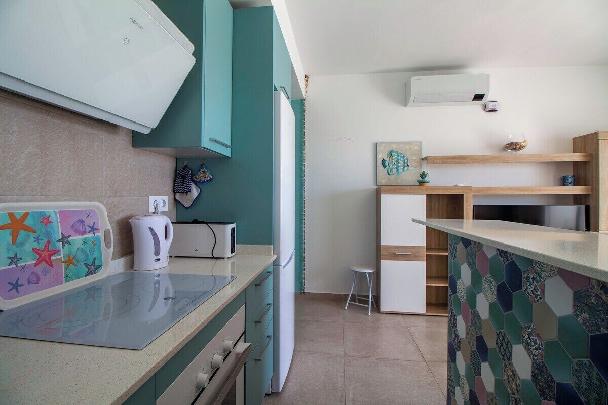 A compact kitchen with a microwave, kettle, and a small stool.