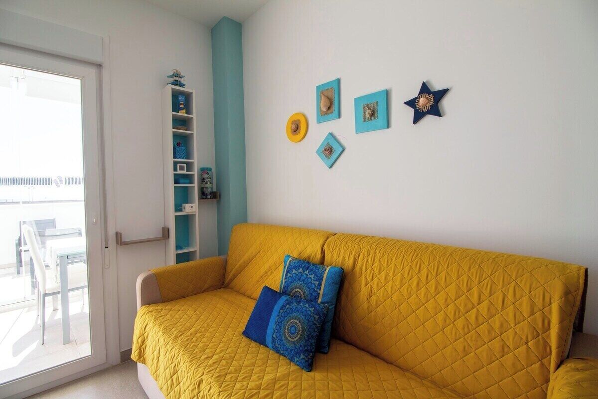 A room with a yellow quilted sofa, a white door, and a blue wall with decorative items.