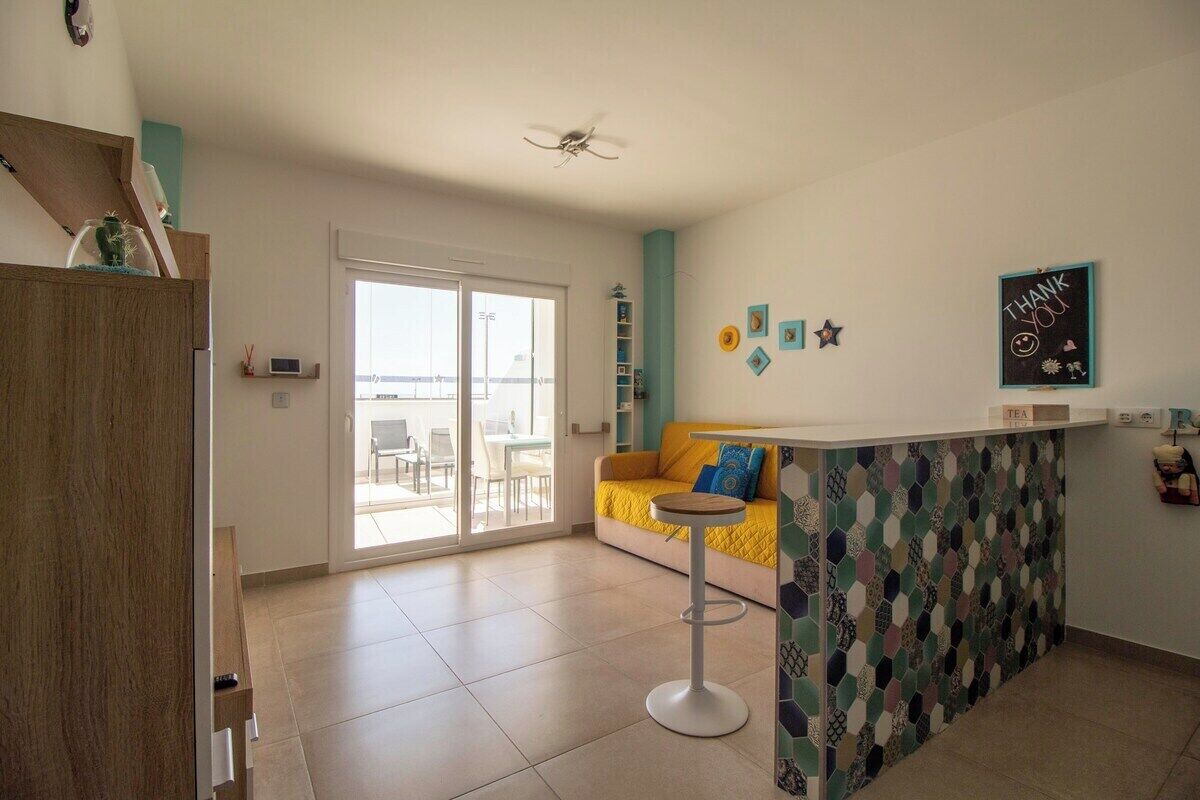 Een moderne keuken met een bar, een schuifdeur naar een balkon en een gele bank.