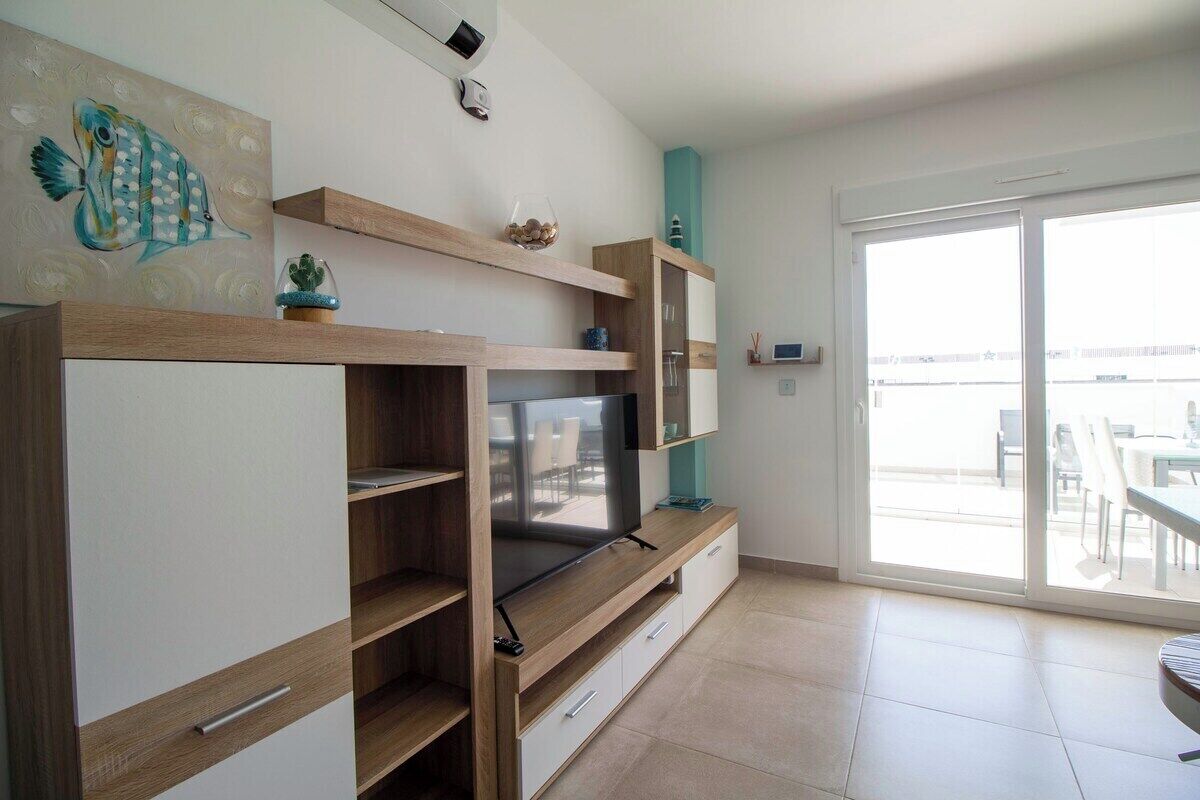 A modern living room with a flat-screen TV, wooden shelves, and a sliding glass door to an outdoor area.