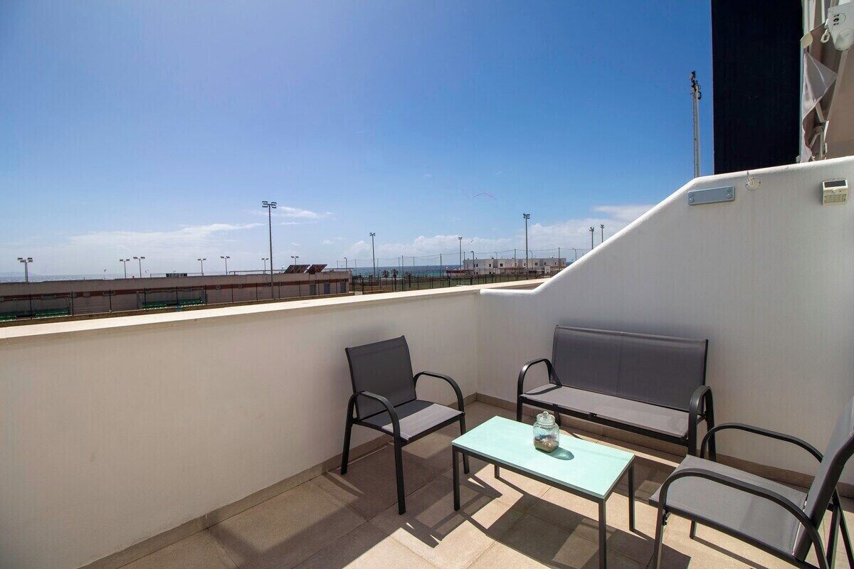 A balcony with two chairs, a table, and a view of the beach and cityscape.