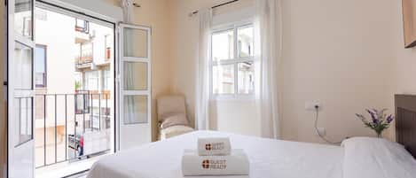 A hotel room with a bed, a chair, a window, and a view of the outside balcony.
