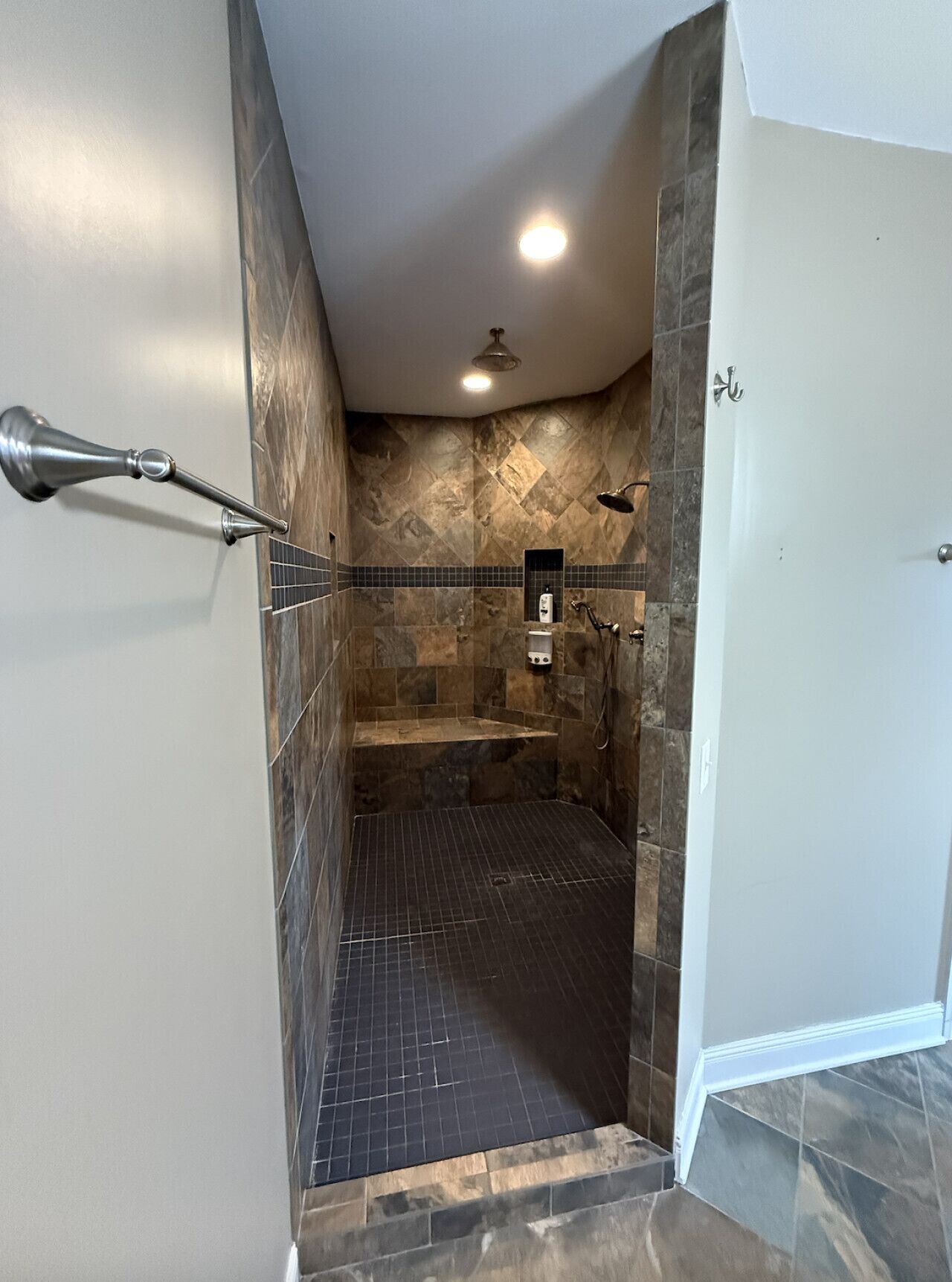 Une douche à l’italienne avec un sol carrelé, une douchette à main et un luminaire fixé au mur.