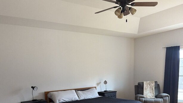 Ein Schlafzimmer mit Bett, Stuhl, Schreibtisch und Deckenventilator.