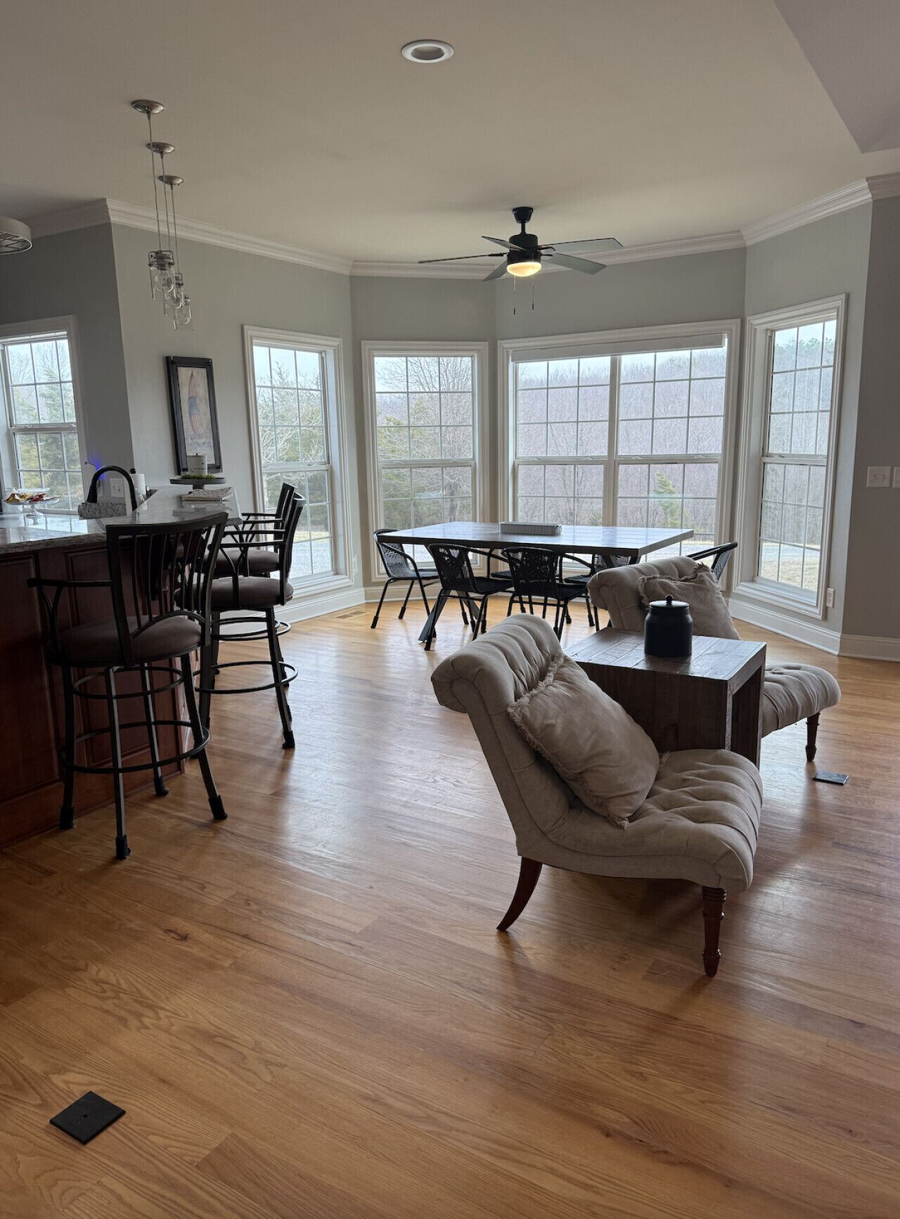 A spacious kitchen with a dining area, large windows, and a ceiling fan.