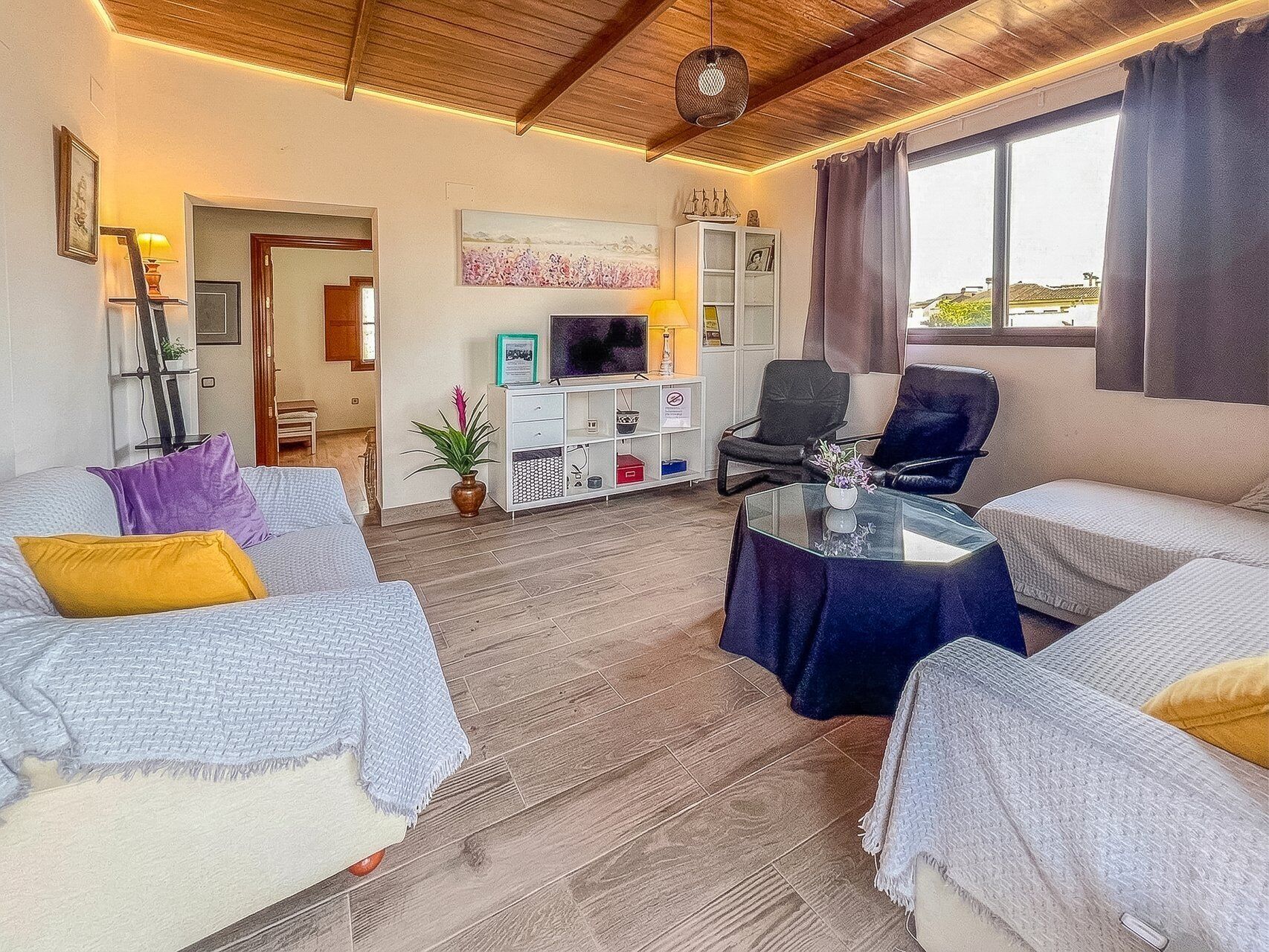Een woonkamer met een bank, fauteuils, een salontafel, een televisie en een boekenkast.