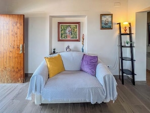 Ein Zimmer mit einer Couch, einer Holztür, einem gerahmten Bild und einem Regal mit einer Lampe.